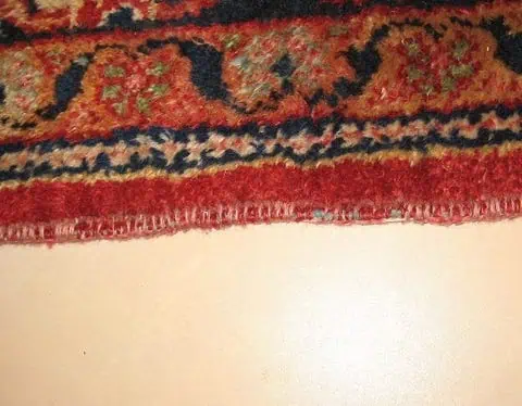 Oud Perzisch tapijt met gerafelde en beschadigde randen, voor reparatie.
